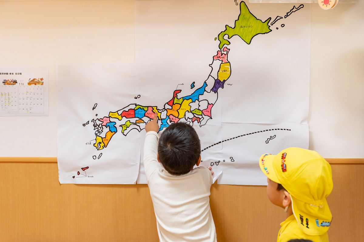 日本の地図を指さして「ここは何県だよ！」。地域や文化などにも自然に興味が持てるよう壁面も工夫している
